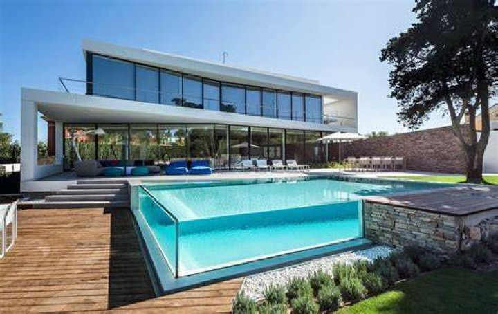 A glass swimming pool and sunken sofa are located in the garden