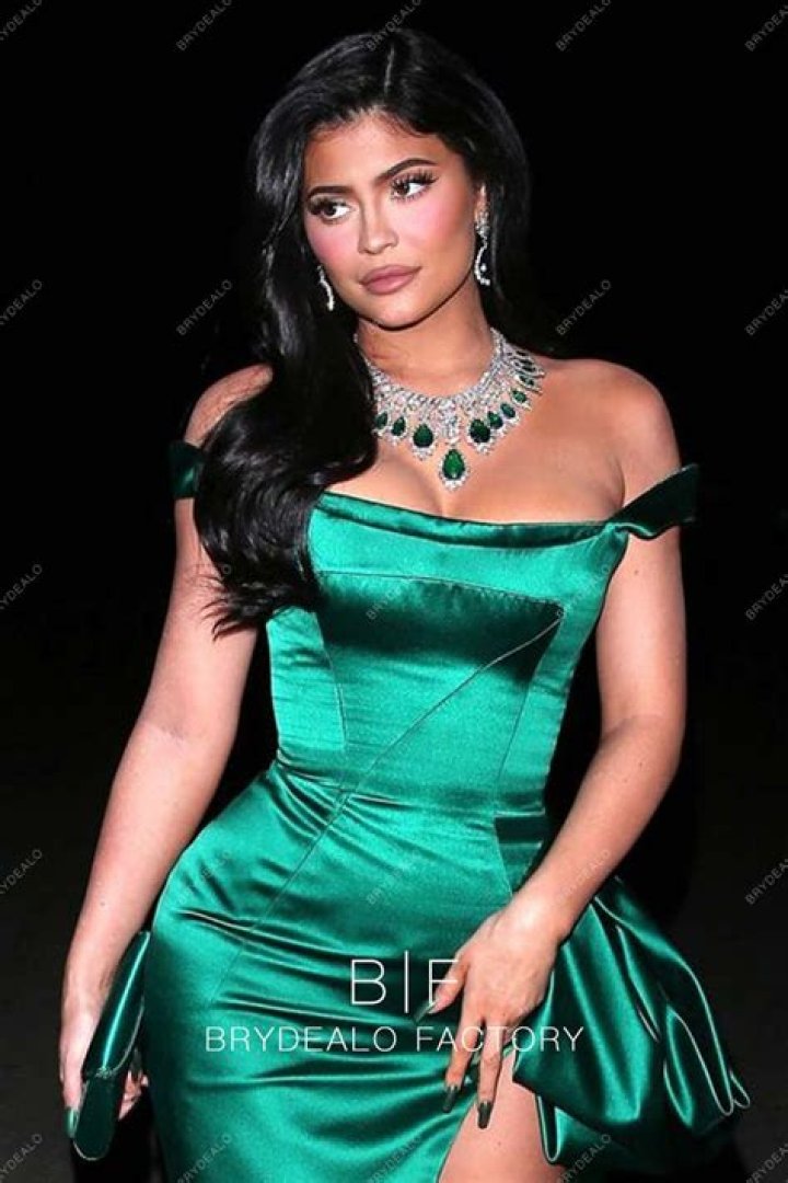 Kylie posed in a green dress against a picture of a garden hung on a brick wall